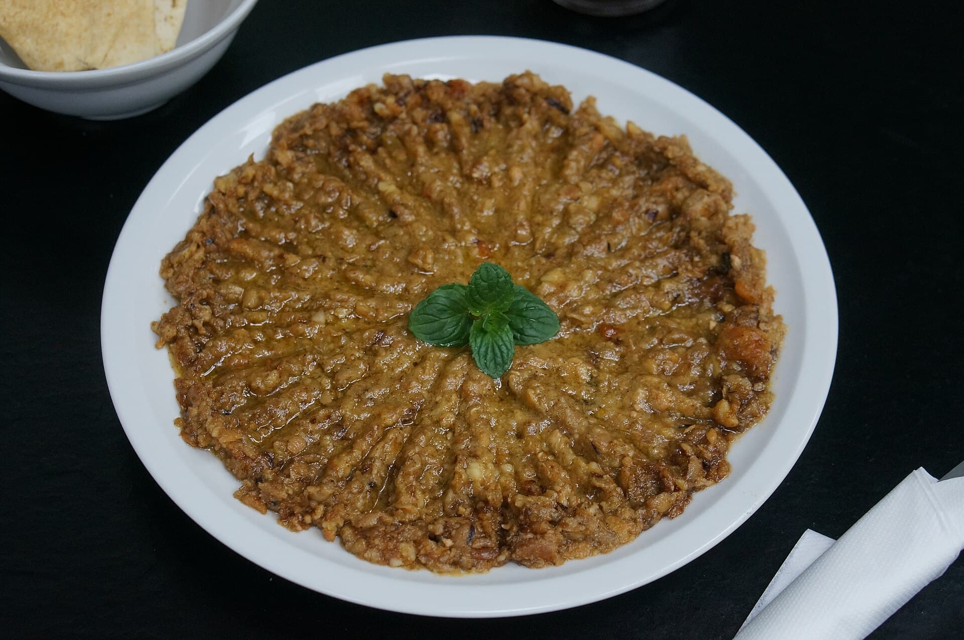 Ein Teller zerdrückter Ful medames mit Petersilie obenauf.