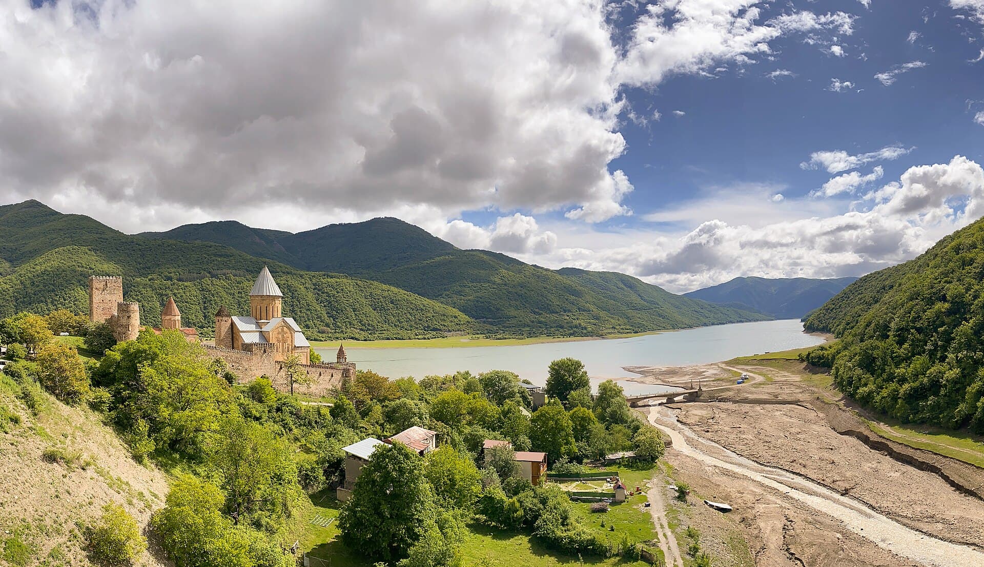Die Festung Ananuri mit Türmen und Kirche am Seeufer zwischen bewaldeten Bergen.