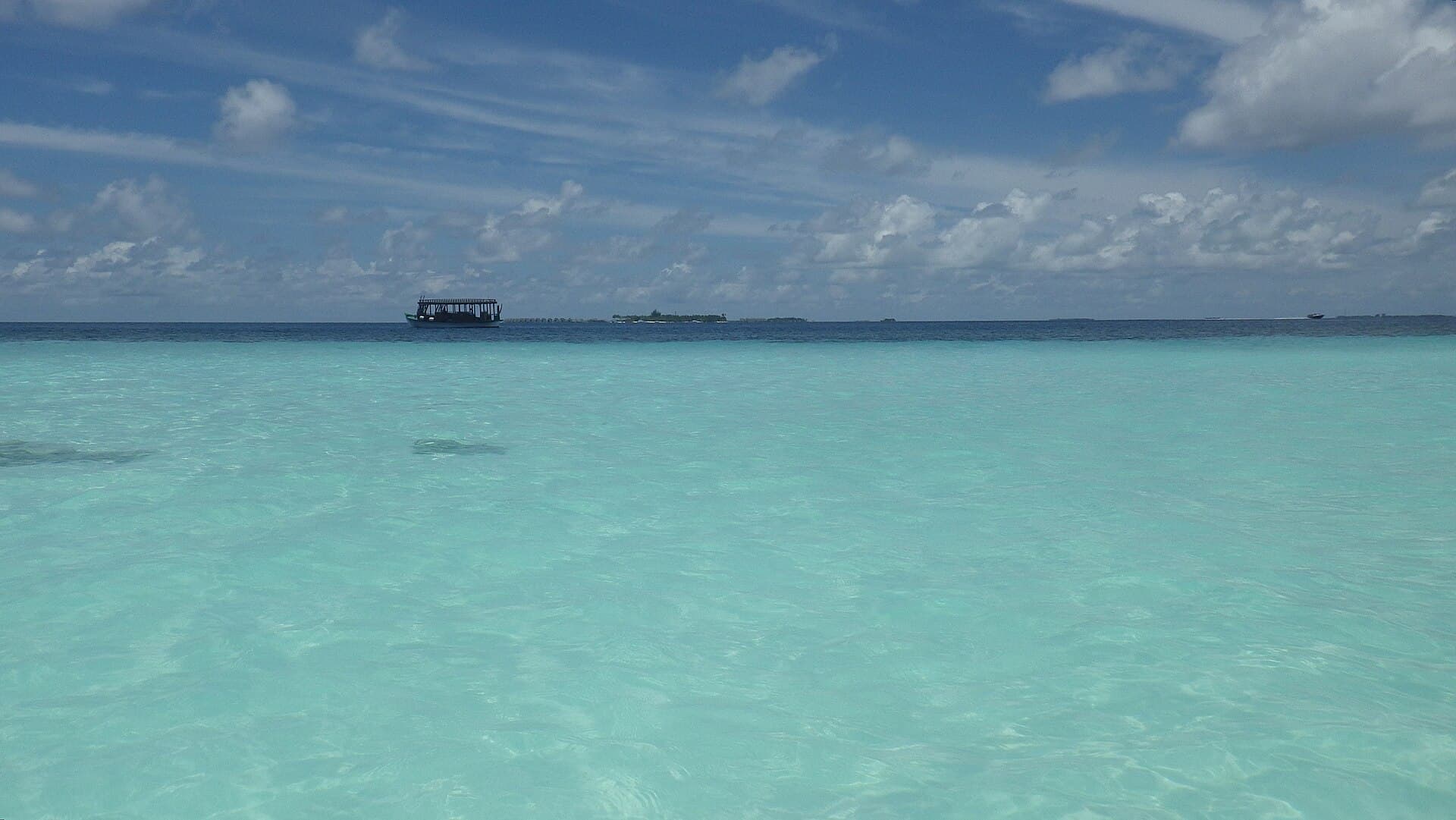 Ein Boot in türkisfarbenem Wasser nahe einer niedrigen Insel im Archipel.