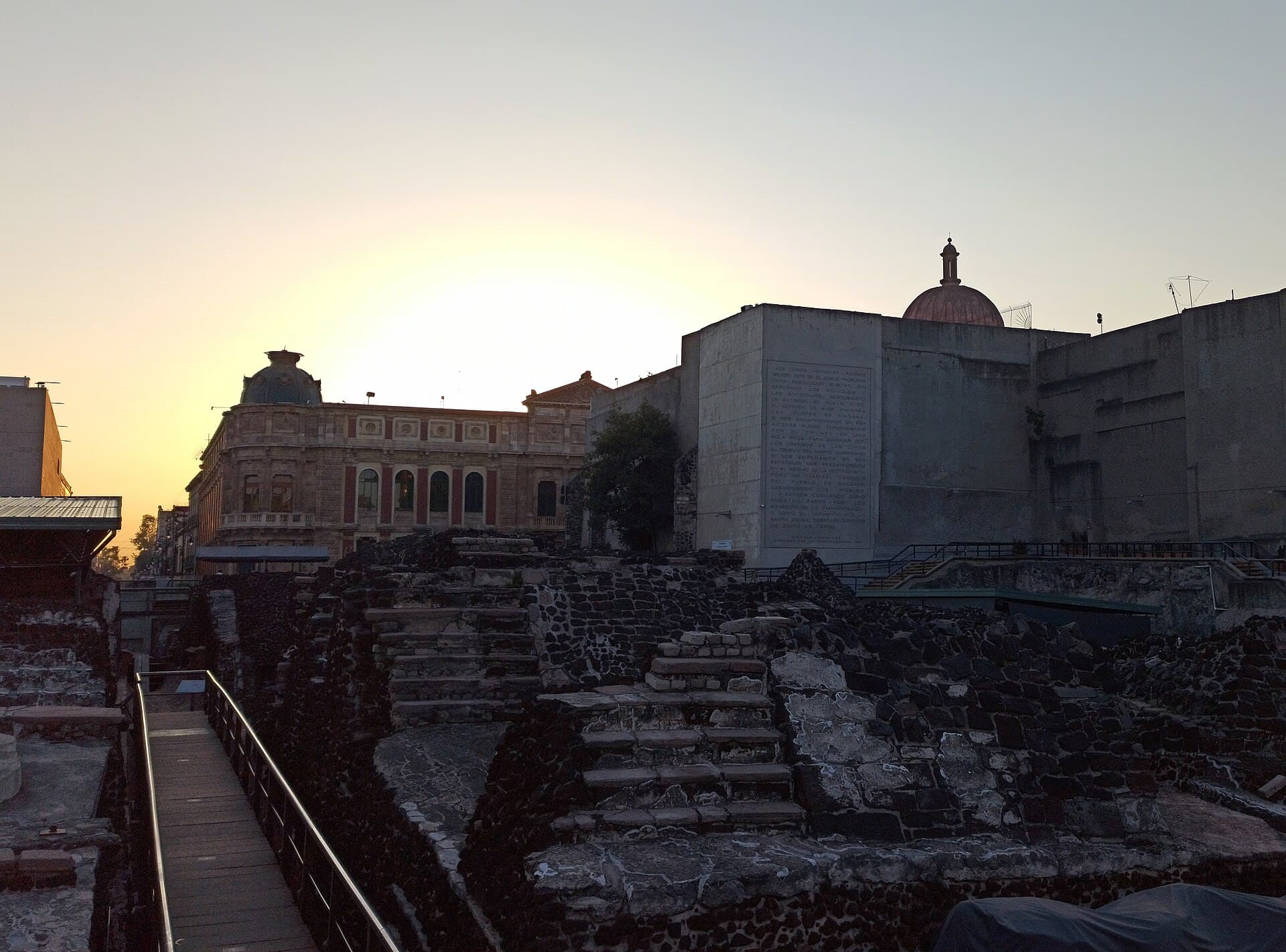 Stone ruins of Tenochtitlan's great temple among colonial buildings in central Mexico City at sunset.