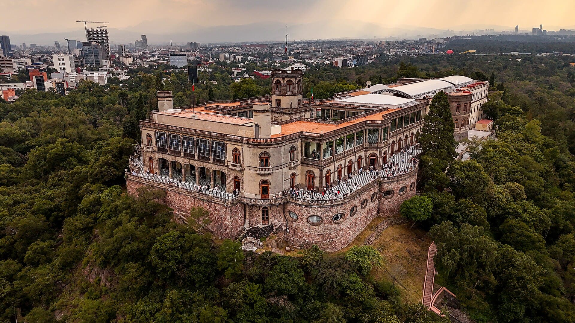 Aerial view of Chapultepec Castle on a forested hill, with the city spreading out behind it.