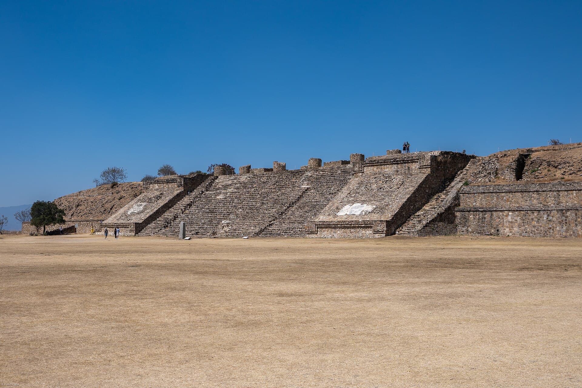 Gestufte Steinplattformen rund um die Große Plaza von Monte Albán unter klarem Himmel.
