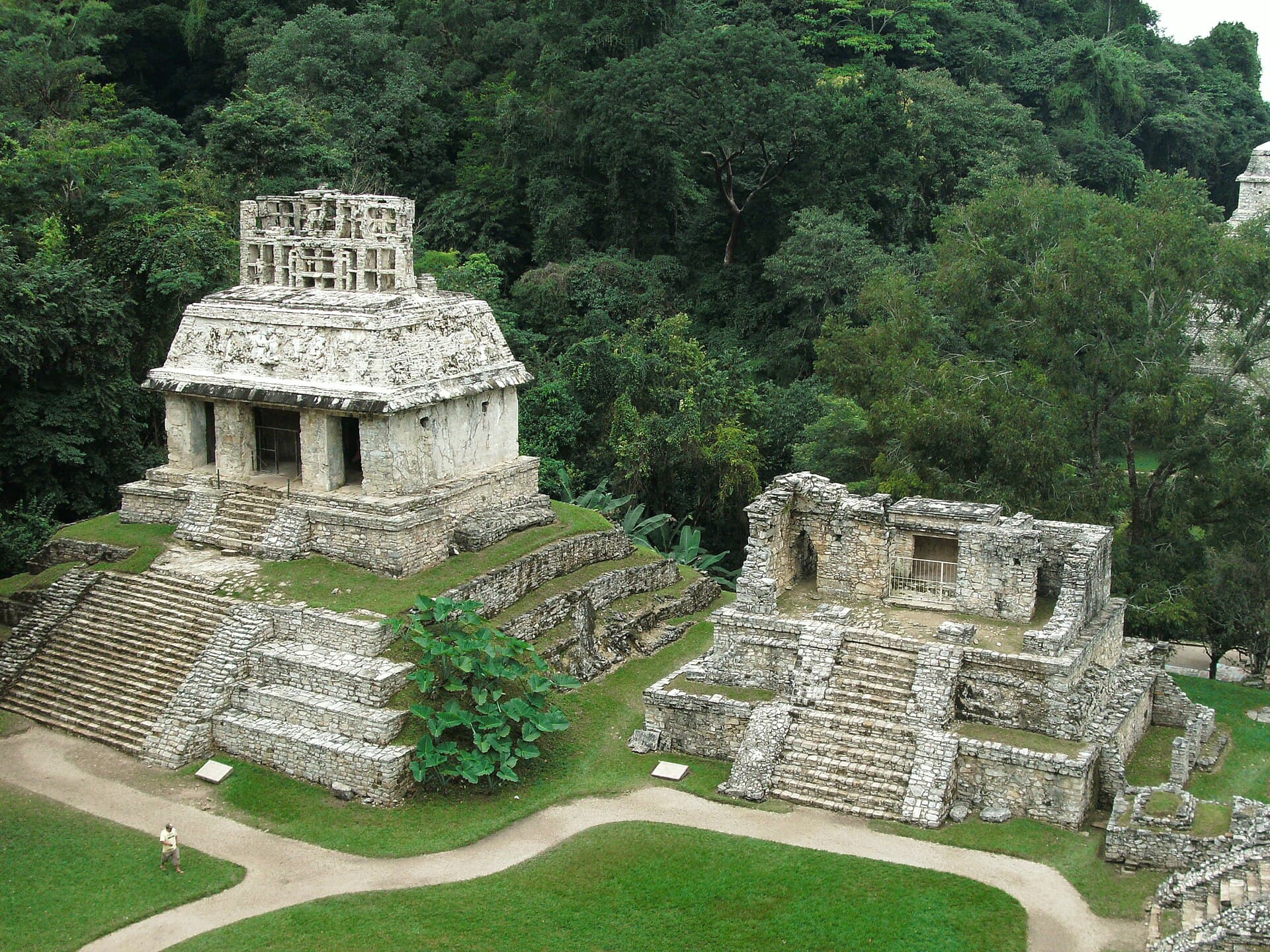 Zwei Tempel der Kreuzgruppe in Palenque auf gestuften Plattformen vor dem Wald.