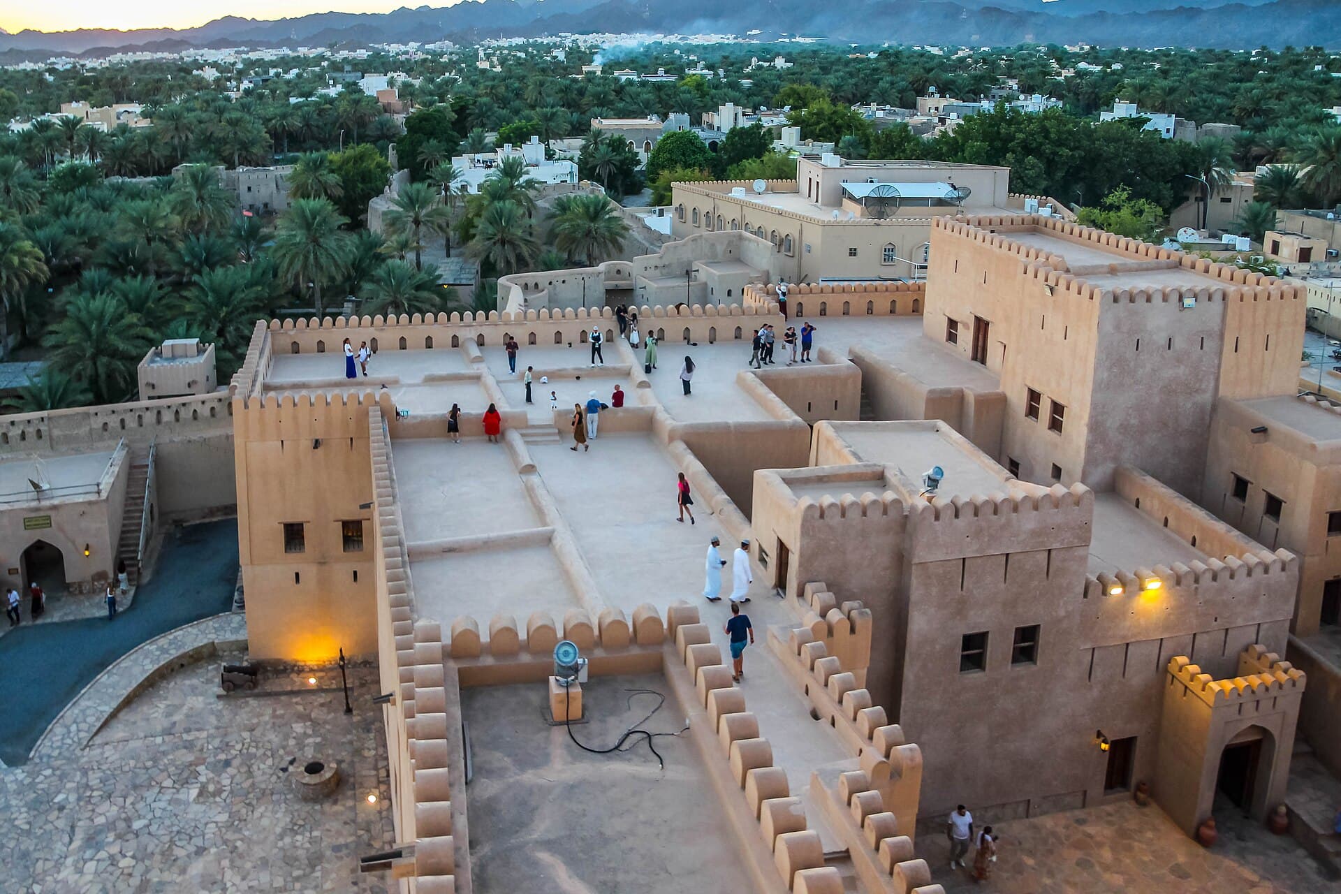 Höfe und Türme der Festung Nizwa von oben, dahinter Palmenhaine.