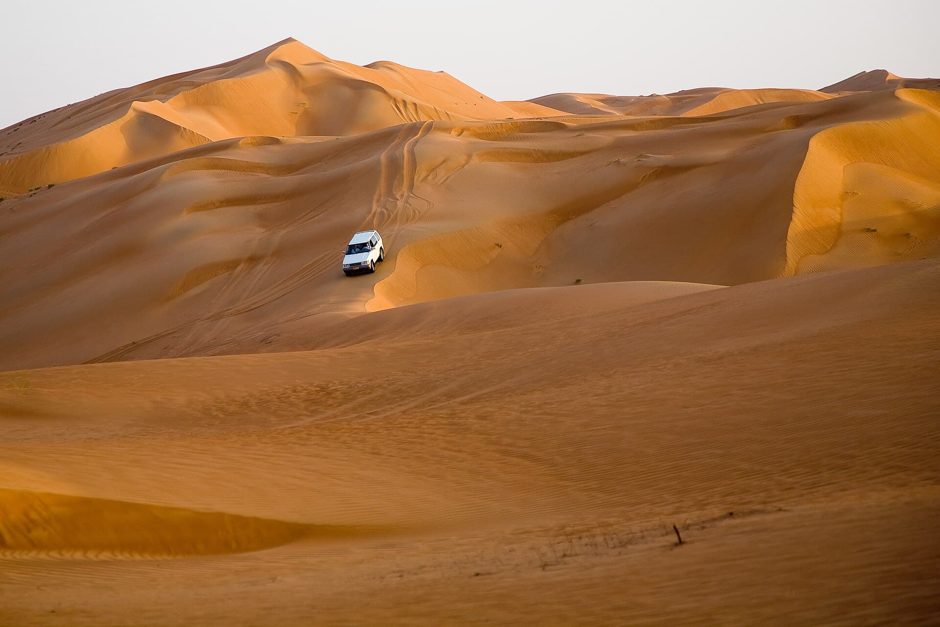 Tall dunes and their shadows in the Sharqiya Sands, with a small car among them.