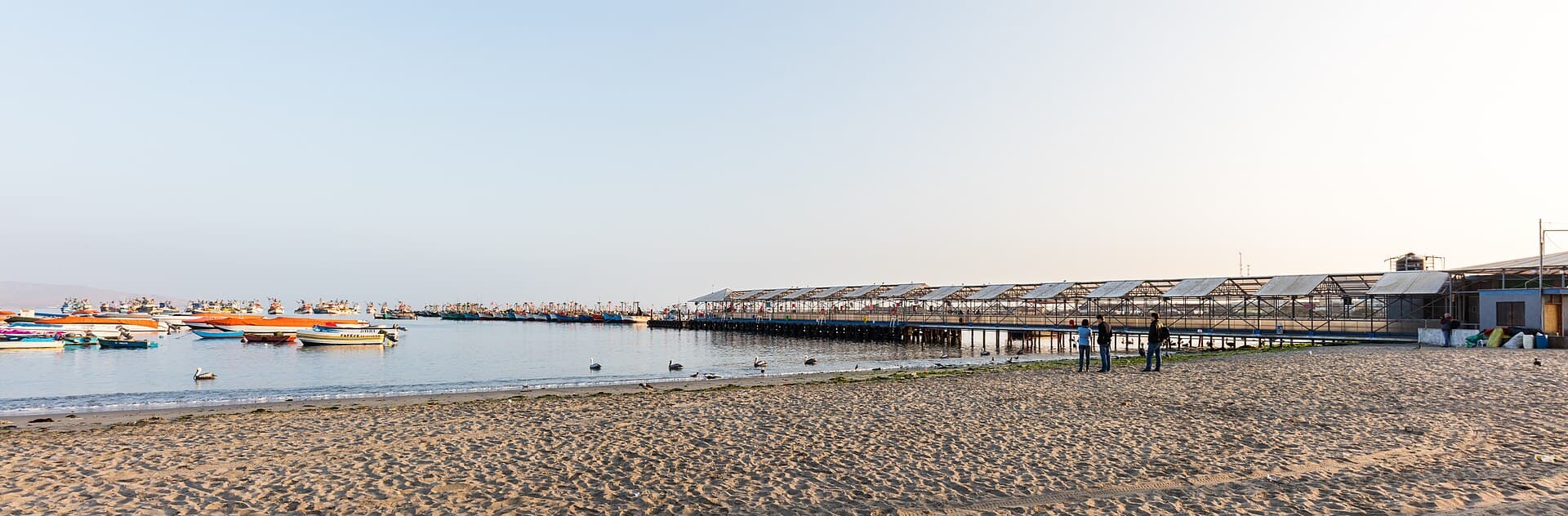 Strand, Steg und Boote im Hafen von Paracas im Morgenlicht.