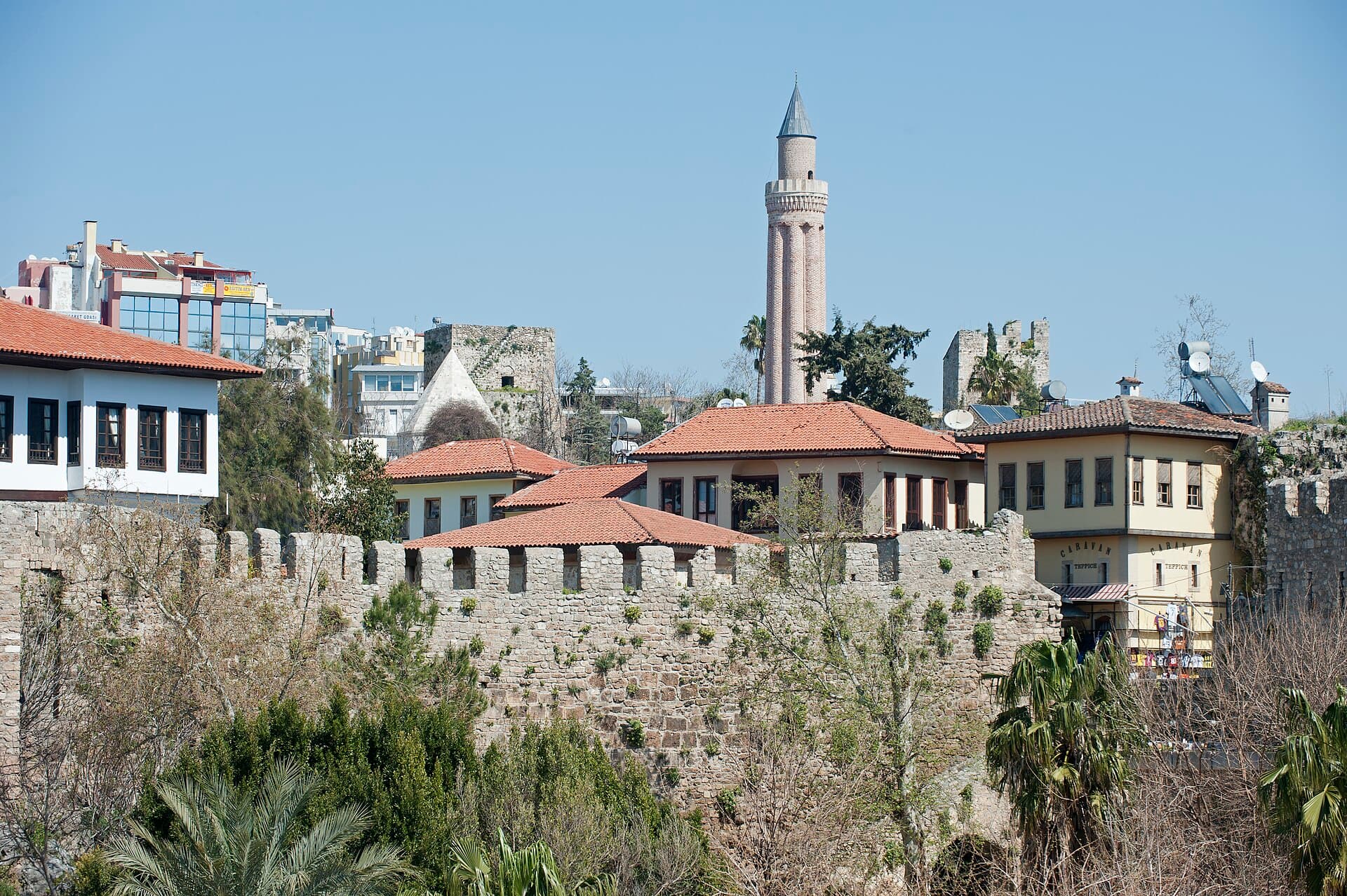 Die Steinmauern von Kaleiçi und Häuser mit roten Dächern, dahinter ein geripptes Minarett.