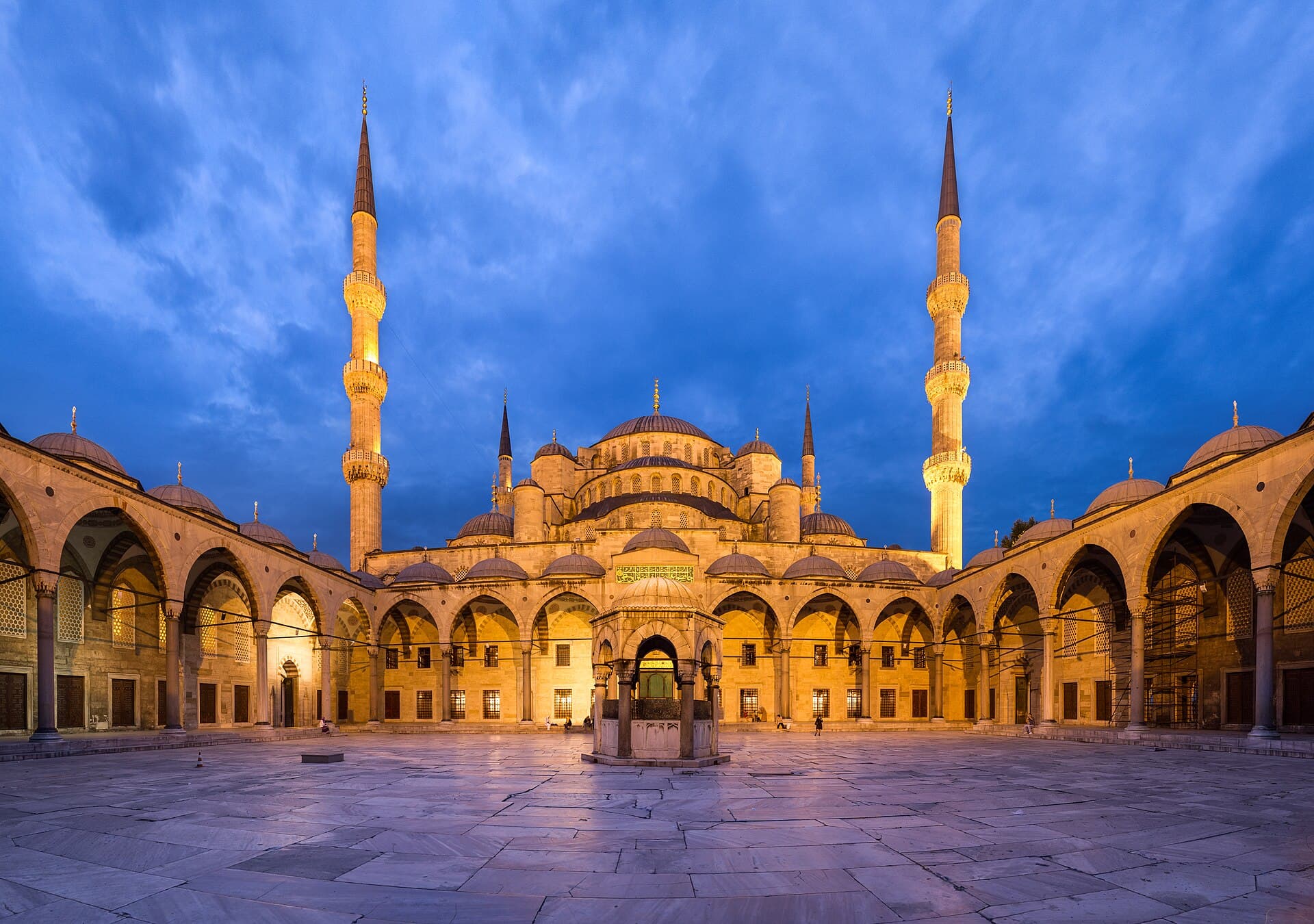 صحن الجامع الأزرق وأروقته المقببة عند الغسق، وقبته ومآذنه مضاءة.