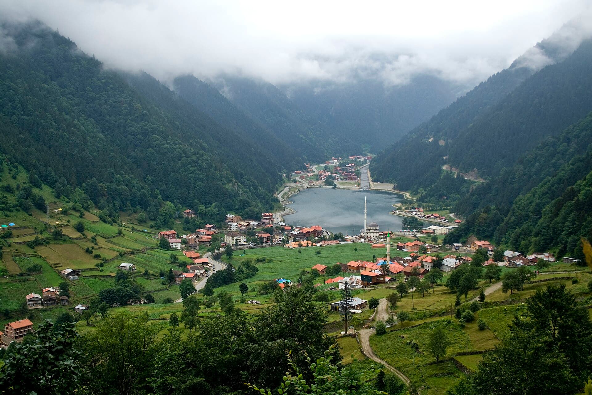 Der See Uzungöl und sein Dorf auf dem Grund eines grünen Tals zwischen wolkenverhangenen Bergen.