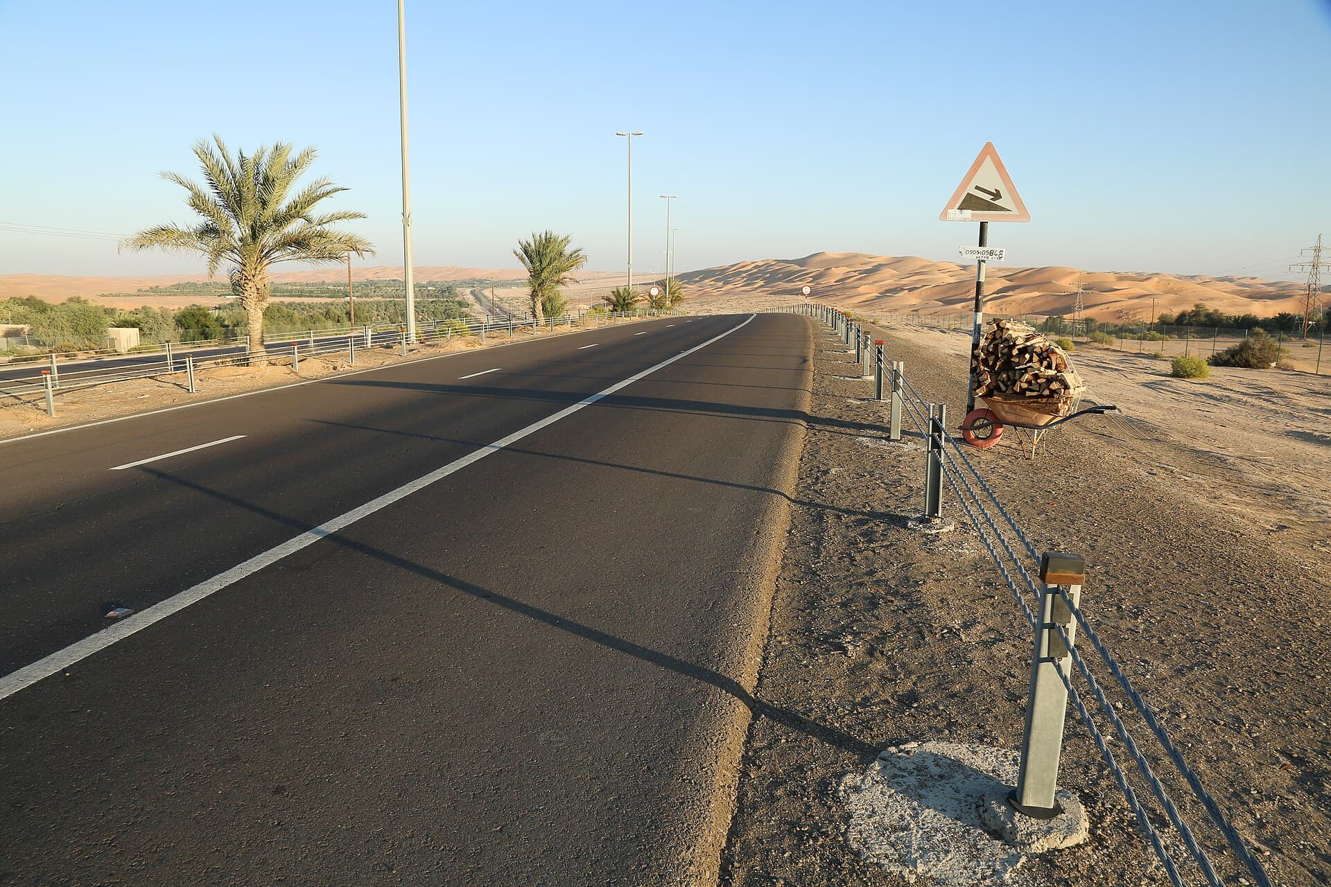 Eine Straße zwischen den Palmen der Oase Liwa und den Dünen.