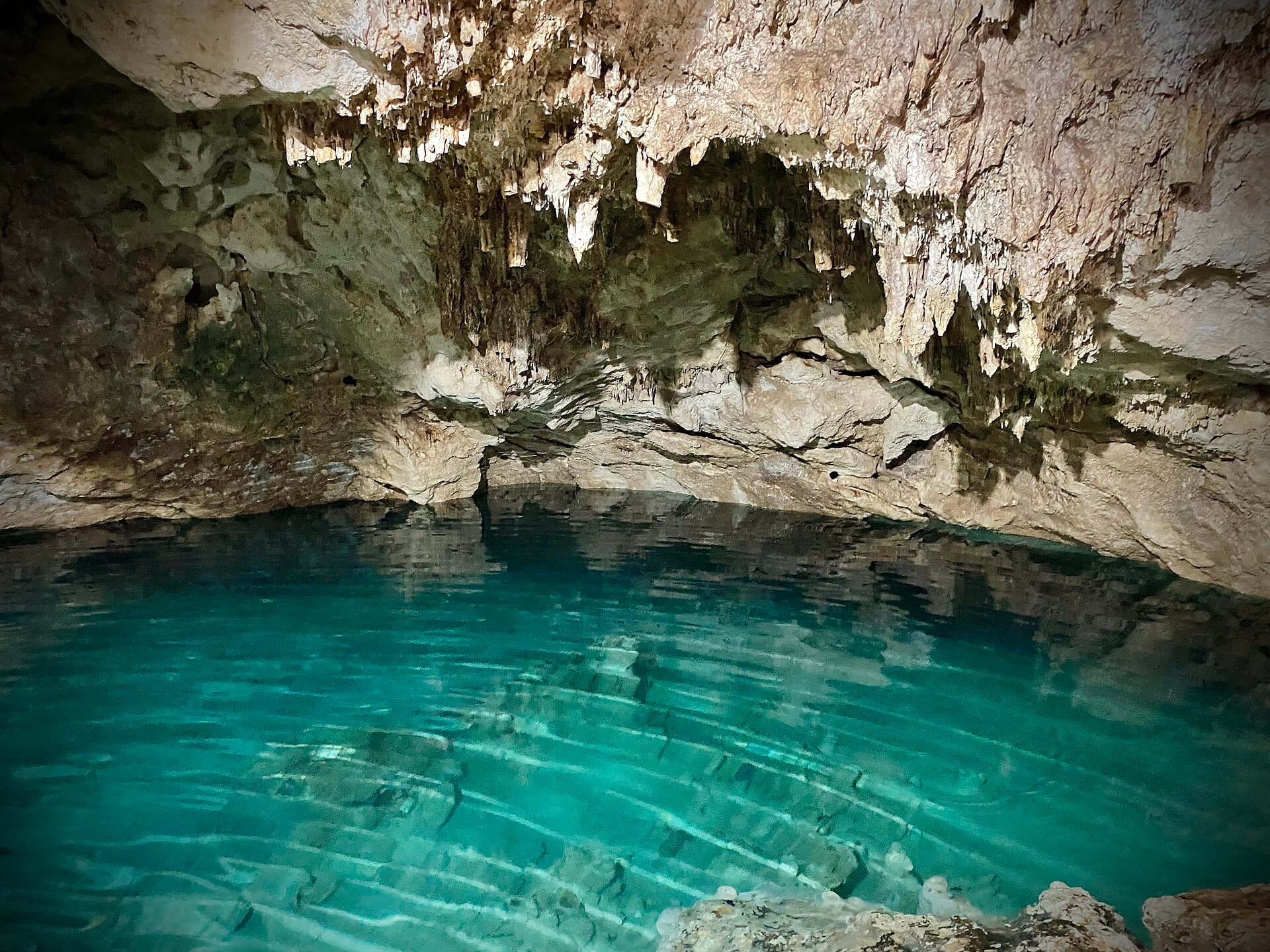 Eine Höhlencenote in Homún, Tropfsteine hängen über klarem, türkisem Wasser.