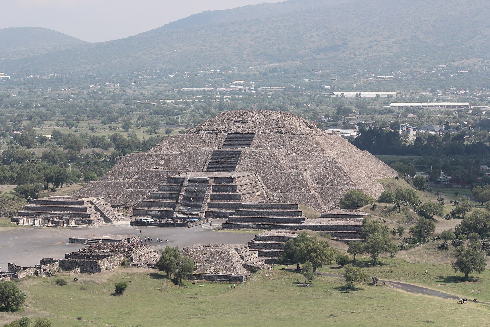 Die gestufte Mondpyramide in Teotihuacan vor einem grünen Hügel.
