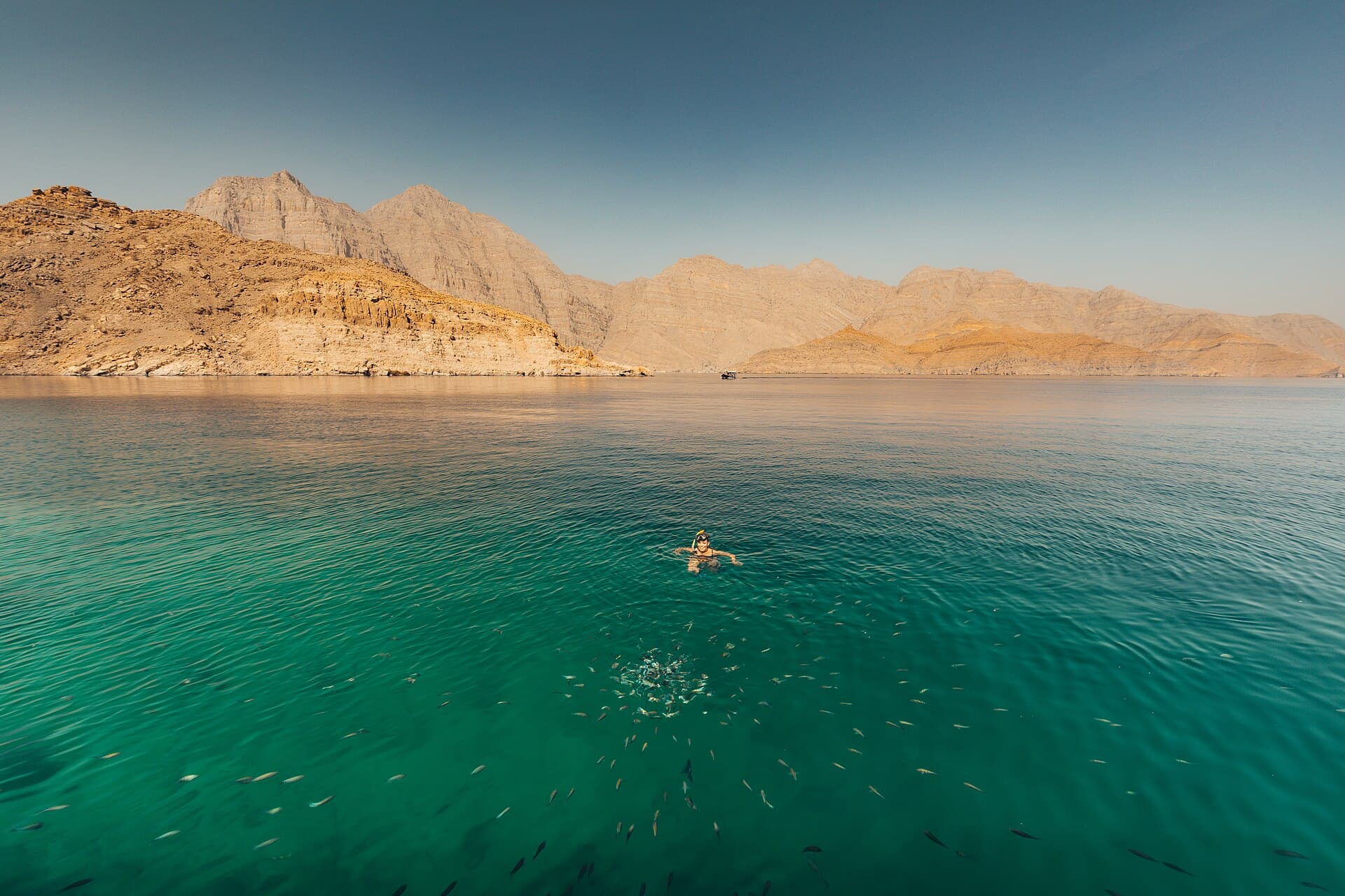 Clear turquoise water in Khor Ash Sham beneath rocky mountains.