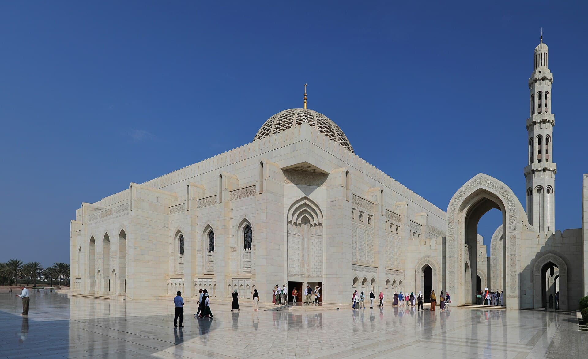 The white stone façade and minaret of the Sultan Qaboos Grand Mosque against a clear blue sky.