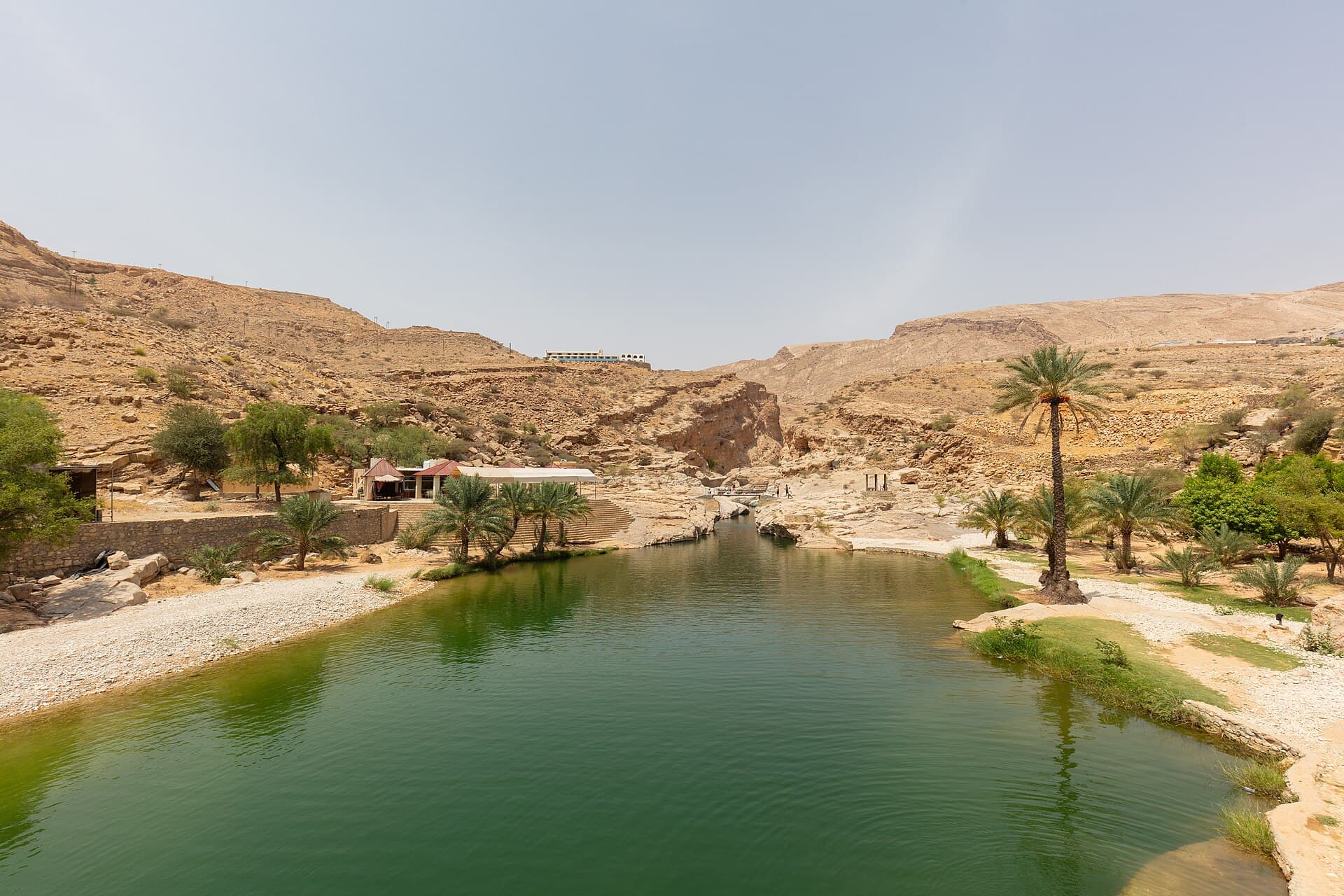 A green pool in Wadi Bani Khalid between pale rocks and palm trees.