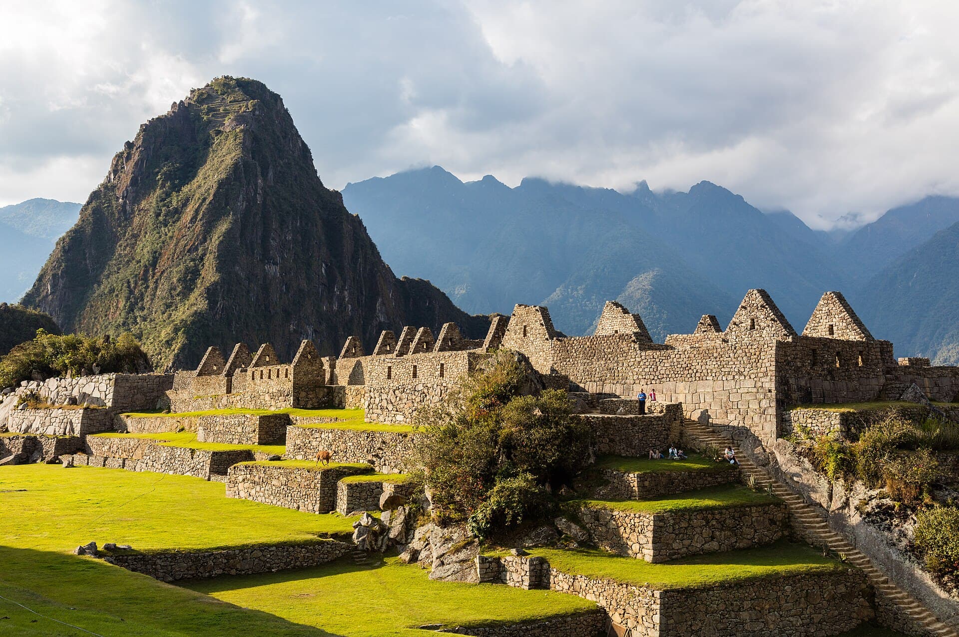 Stone buildings and green terraces at Machu Picchu, with the sharp peak of Huayna Picchu behind.